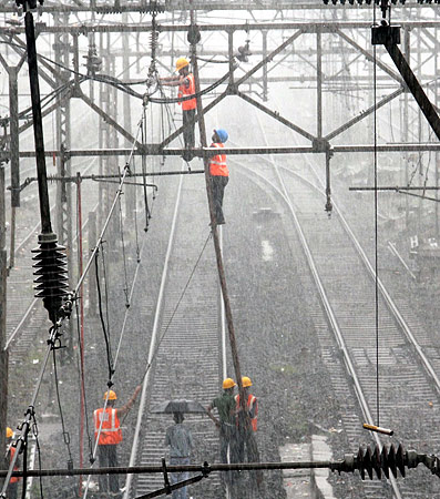 Railway workers are seen working on overhead wires amid heavy rains