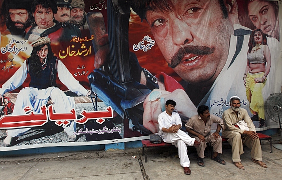 Cinema workers sit near a poster of a Pashto movie at Arshad cinema in Peshawar