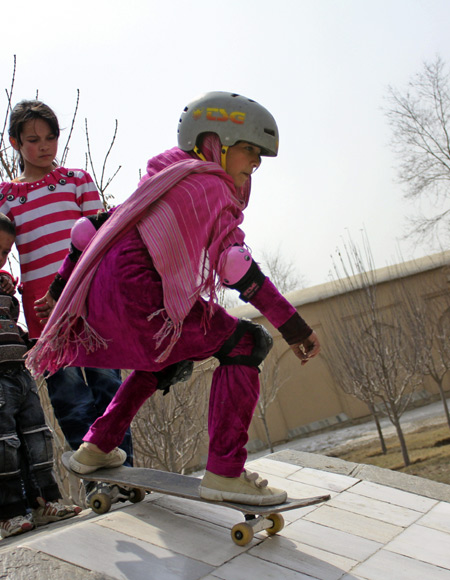 Wearing helmet and knee guards, a girl tries some new skateboarding tricks in Kabul, Afghanistan