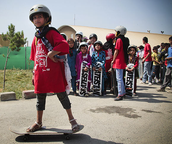 An Aghan teenage girl tries balancing on the skateboard during a session while others await their turn