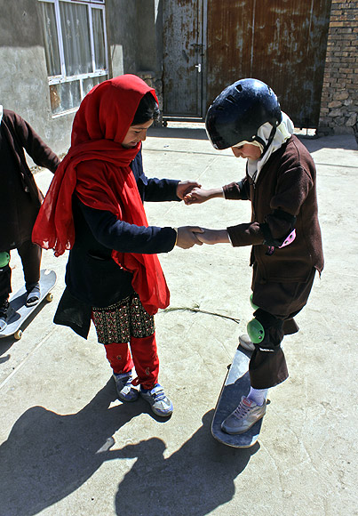 An Afghan girl helps her friend to learn skating in Kabul
