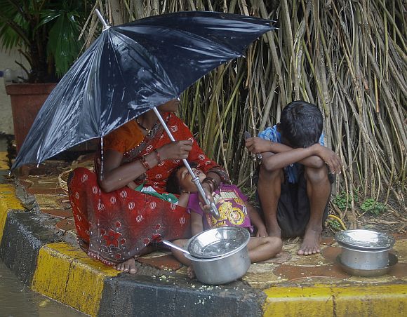 A woman holds an umbrella to shield her children and herself from the rain along a roadside in Mumbai