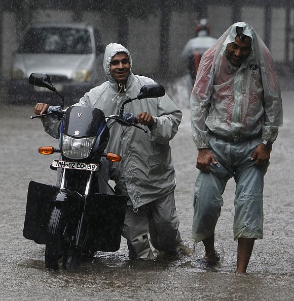 A man pushes his stalled motorcycle through a flooded street as his friend walks with him during monsoon rains in Mumbai