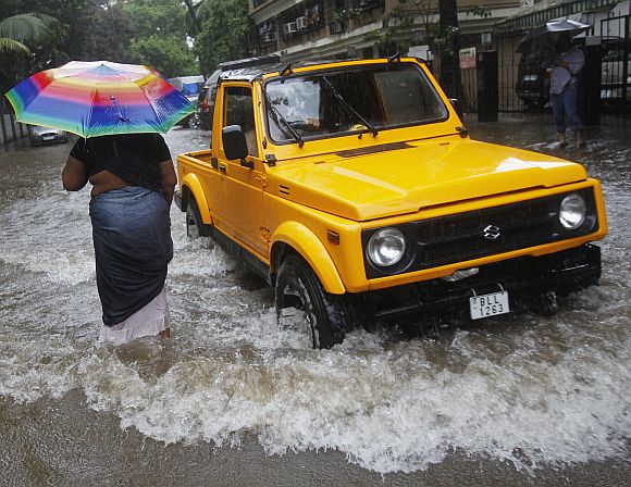 A woman walks through a flooded street as as a four-wheel drive vehicle passes her during monsoon rains in Mumbai