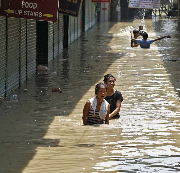 Girls wade through a flooded alley at a shopping arcade after heavy monsoon rains caused the rise in waters of Yamuna river in New Delhi