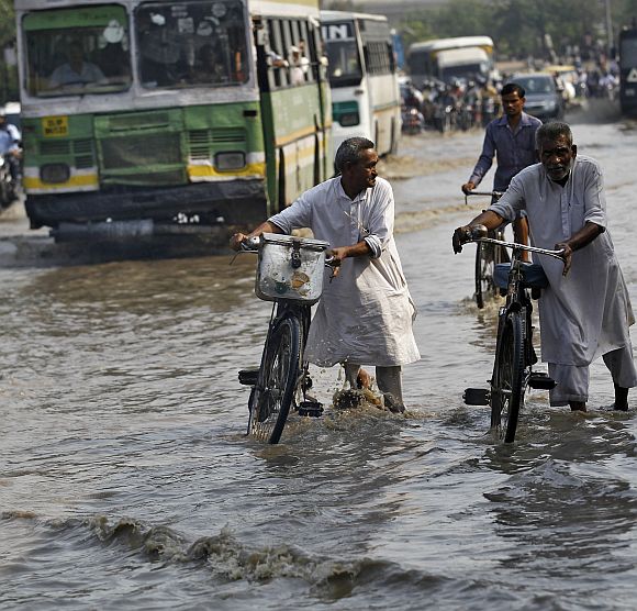 Commuters push their bicycles through a flooded road after heavy monsoon rains caused the rise in waters of Yamuna river in New Delhi