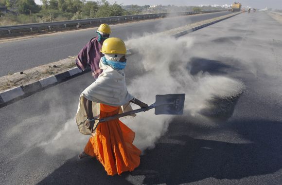 A woman labourer spreads black ash over a newly constructed road at Raipur village, in Gujarat