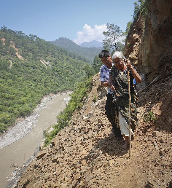 A pilgrim is helped by a villager as she tries to cross on a pathway damaged by landslide in Rudraprayag in the Himalayan state of Uttarakhand