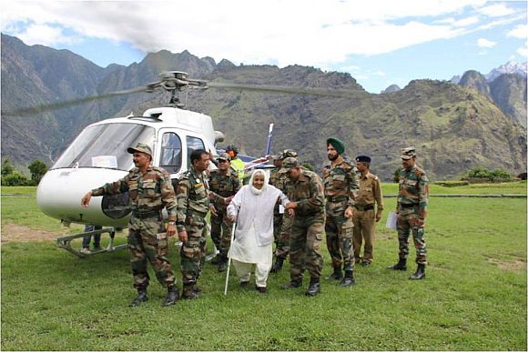 An elderly lady being escorted by Indian Army soldiers from a helicopter