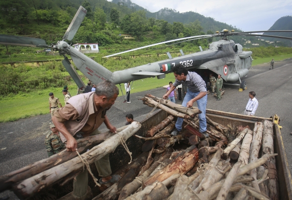 Volunteers unload wood from a truck to be used for mass cremation at Kedarnath at an airport in Gauchar