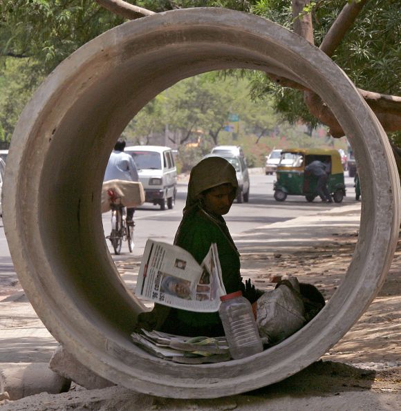 A homeless woman takes cover from the sun in a pipe as she fans her baby