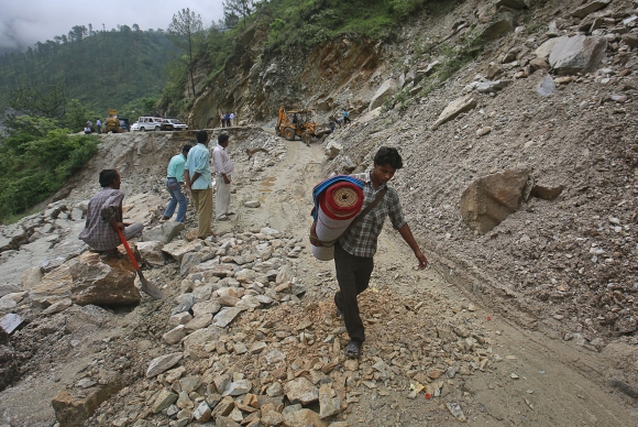 A villager crosses a road damaged by a landslide due to heavy rainfall in Gauchar