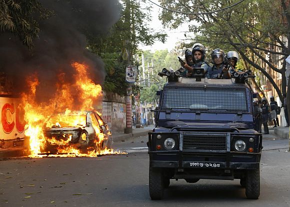 A police van passes a burnt vehicle after activists of Bangladesh Nationalist Party (BNP) set fire to it during a clash in Dhaka