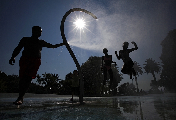 Children play under a shower in a public garden to cool off in the summer heat in Nice