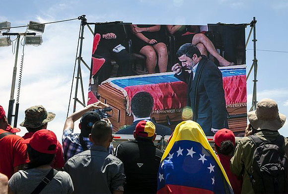 Supporters of Hugo Chavez watch a screen as Mahmoud Ahmadinejad walks past Chavez's coffin during the funeral ceremony