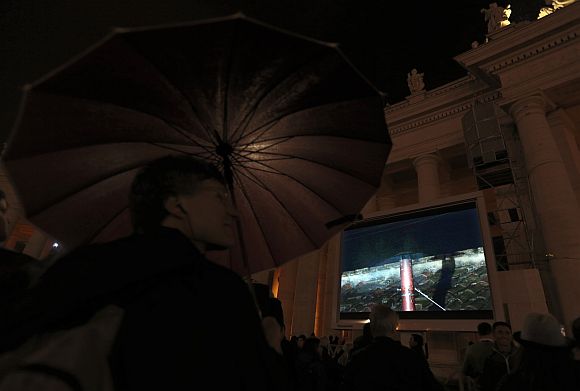 People in Saint Peter's Square watch a live television screen showing black smoke rising from the chimney above the Sistine Chapel, indicating that no decision has been made after the first day of voting