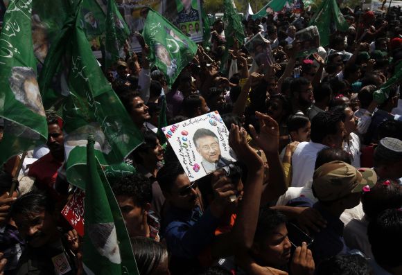 Supporters of Pervez Musharraf carry flags and portraits of their leader as they wait upon his arrival in Karachi