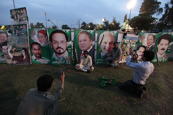 Supporters of the PML-N party take pictures in front of banners of Nawaz Sharif (centre) and other party leaders during an election campaign rally in Rawalpindi