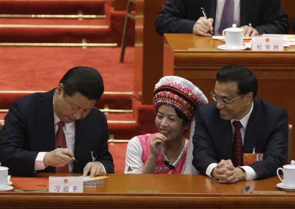 Li Keqiang and an ethnic minority delegate look at China's President Xi Jinping signing an autograph at the Great Hall of the People in Beijing