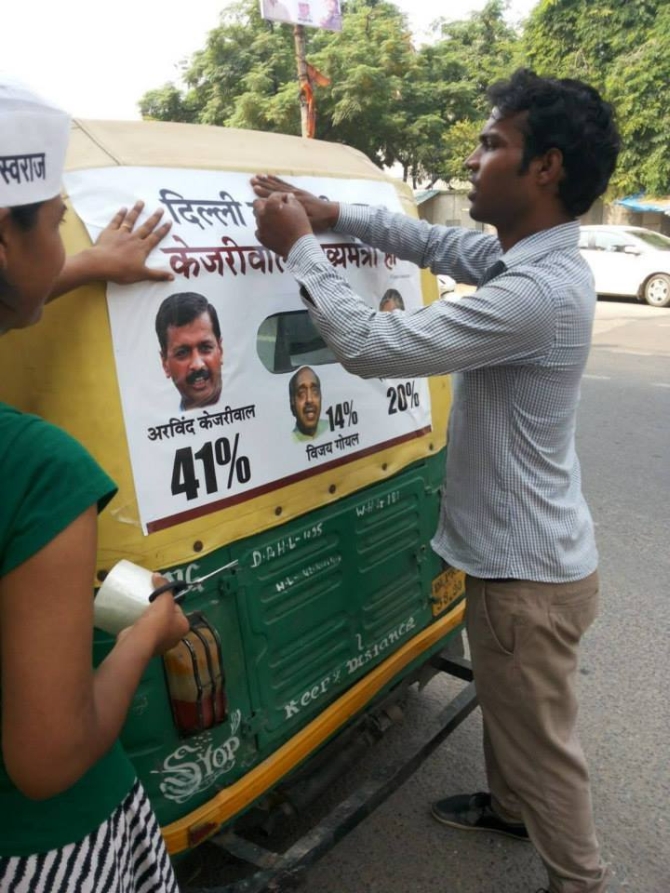 AAP supporters put up posters depicting results of poll surveys on an autorickshaw in Delhi