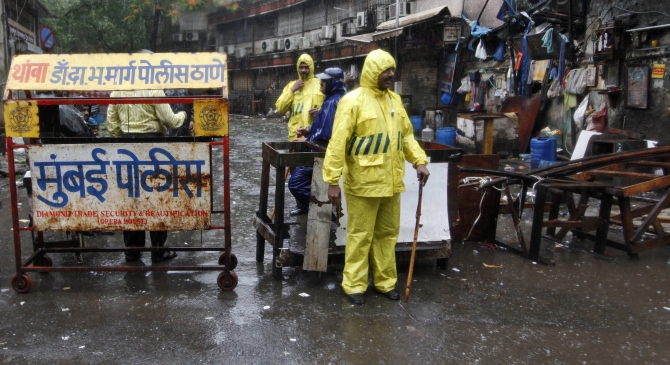 Policemen stand guard in the rain next to a barricade they installed at one of the sites of triple explosions in Mumbai on July 13, 2011, near the Opera House.