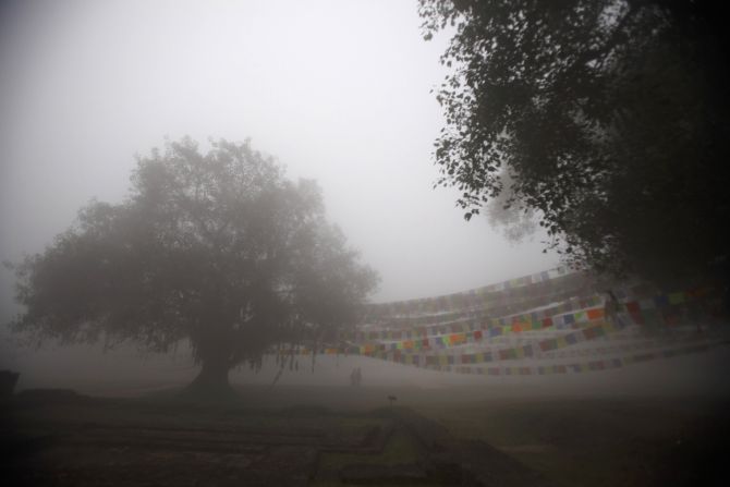 People walk past prayer flags on a foggy morning at the Maya Devi Temple in Lumbini