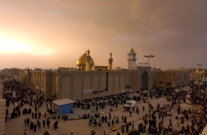 Iraqis walk past the shrine of Imam Ali in Najaf at sunset before a dust storm in Najaf