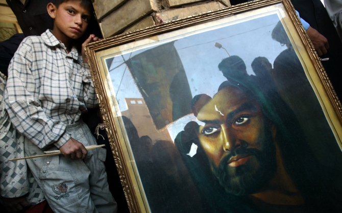 Shiite Muslims are reflected in a portrait of Imam Hussein, the son of Imam Ali outside the shrine of Imam Ali to mark the anniversary of the death of Mohammed in Najaf
