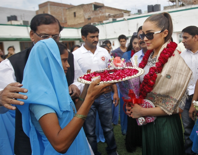 Miss Universe 2012 and Miss USA 2012 Olivia Culpo (R) wearing floral garlands, gets a traditional Indian welcome upon her arrival at a school in New Delhi on Sep