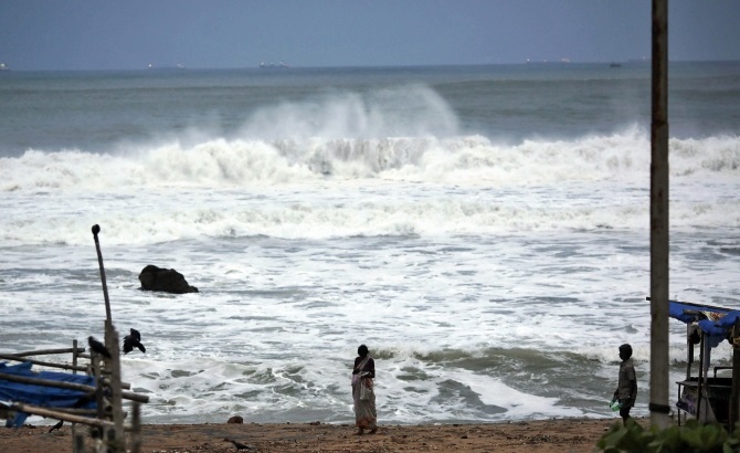 People stand as waves from the Bay of Bengal approach the shore in Visakhapatnam district