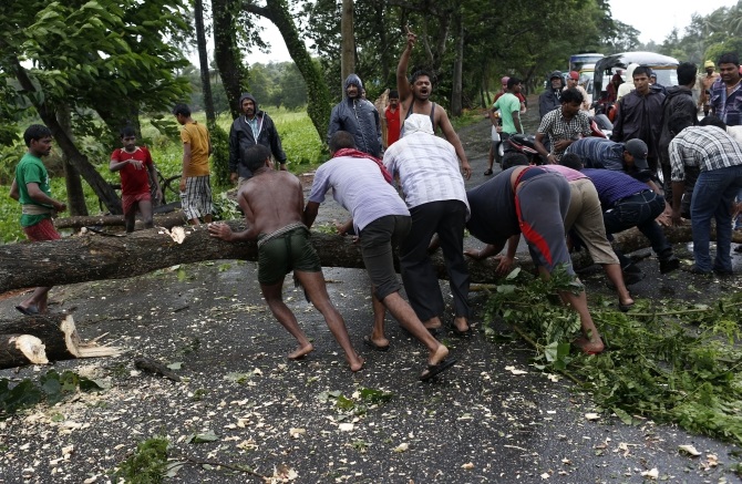 Men try to remove fallen trees from a road due to the rain and wind in Odisha