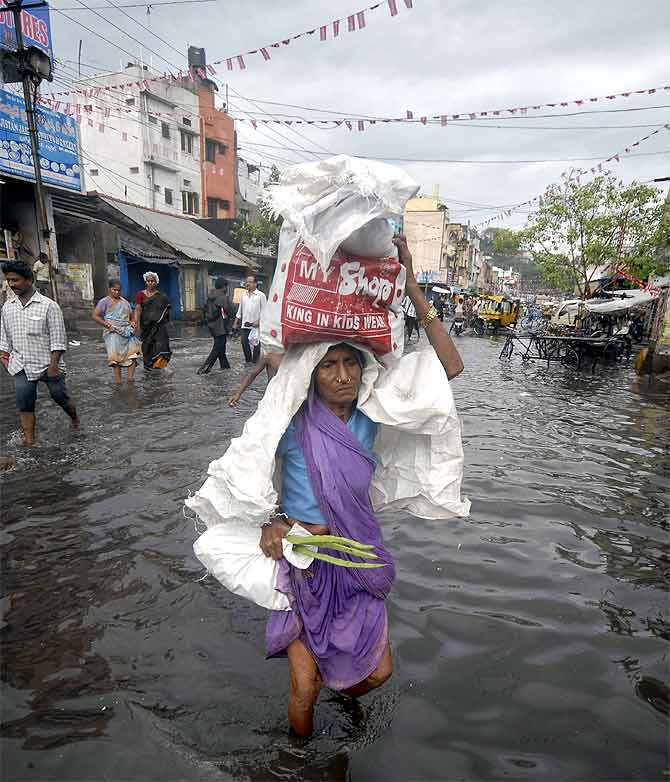 A woman carries a bag as she walks through a flooded street after heavy rains