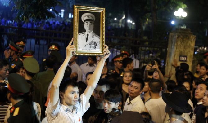 A man holds up a portrait of General Giap while gathering outside his home to pay homage in Hanoi.