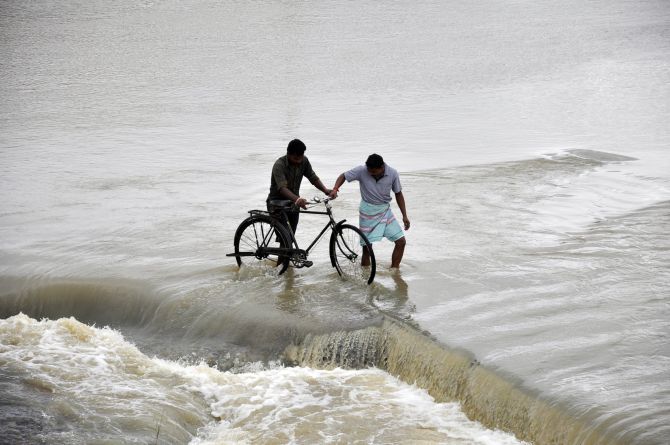 Men cross a flooded road after heavy rains caused by Cyclone Phailin at Gaghra village in Jharkhand