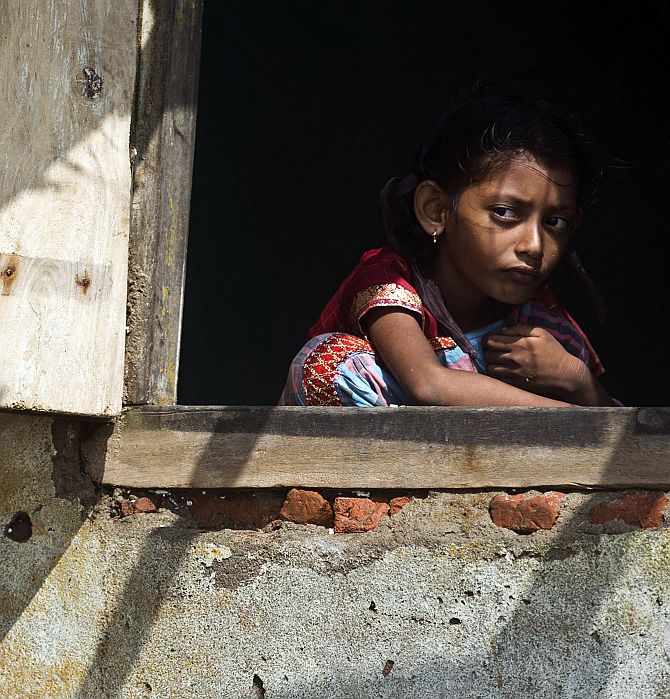 A girl looks out from the window of her partially damaged house