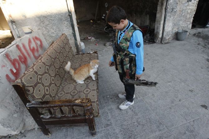 Abboud, 12, plays with a cat while holding his weapon in Aleppo's Sheikh Saeed neighbourhood