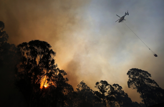 A helicopter carries water to be dropped on a bushfire in Castlereagh, near Sydney