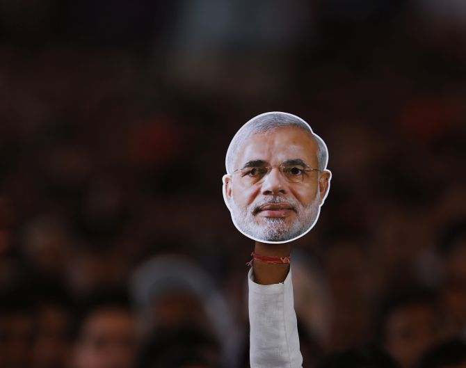 A supporter of BJP holds a mask of Narendra Modi during a campaign rally