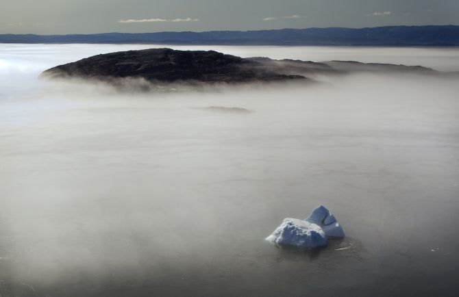 A large iceberg is seen on the edge of a morning fog over Frobisher Bay, Nunavut in the Canadian Arctic