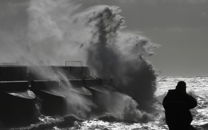 A man watches stormy seas in strong winds as waves crash on the harbour wall at Brighton marina in south east England on Monday