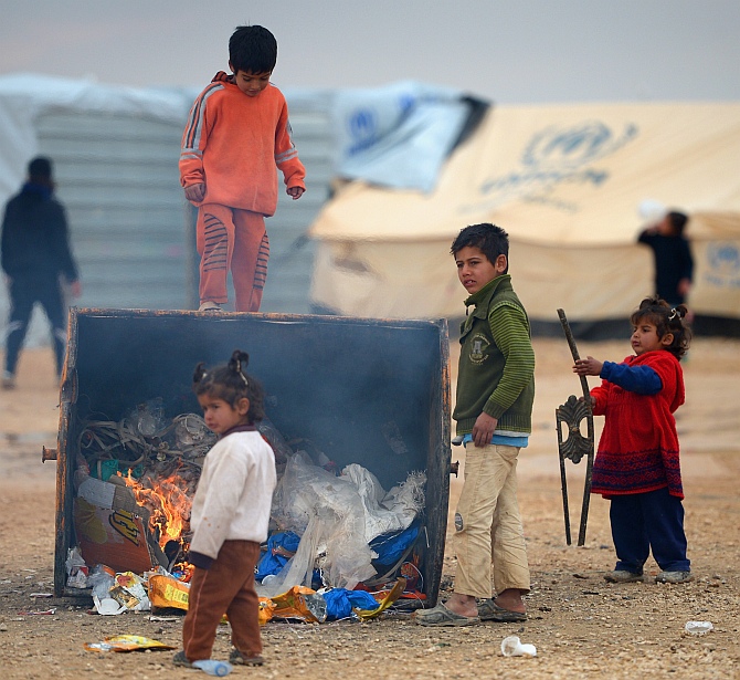 Young children get heat from a burning rubbish bin as Syrian refugees go about their daily business in the Za'atari refugee camp in Jordan