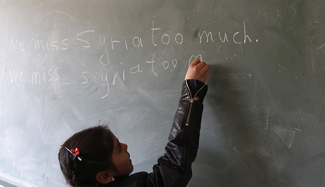 A Syrian refugee girl writes we miss Syria too much on the chalkboard in her classroom in Majdel Anjar in Bekaa Valley