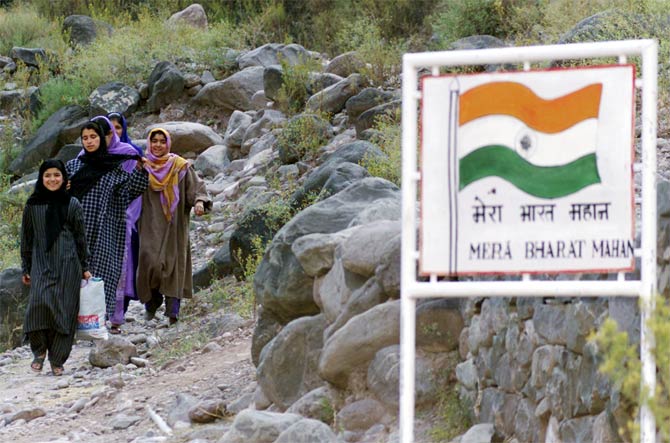 Kashmiri village girls walk near a signboard that reads: 'My India (is) Great'