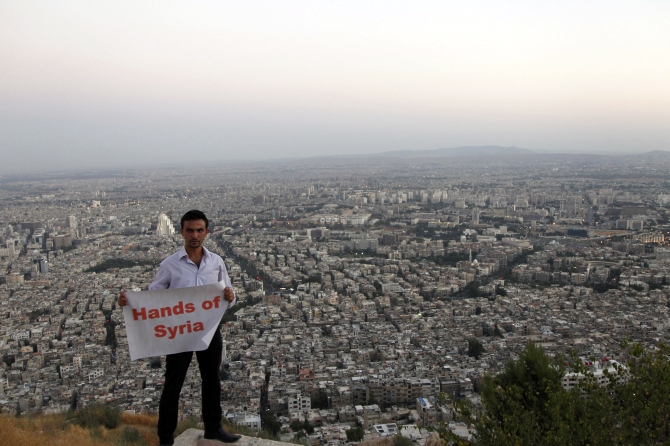 A supporter of Syria's President Bashar al-Assad holds a placard during his participation with others in 'Over our Bodies', a campaign to organise human shields against possible US strikes, at Qasion Mountain overlooking the capital Damascus