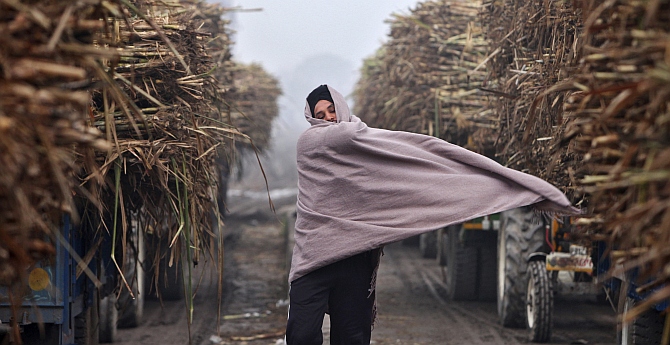 A farmer covers himself with a shawl on a cold winter day outside a sugar mill at Morinda, in Punjab