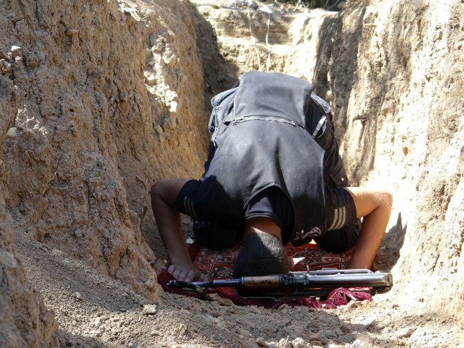 A Free Syrian Army fighter prays near a weapon in a trench in Al-Maliha, Damascus suburbs