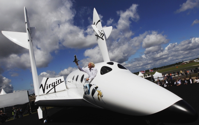 Entrepreneur Richard Branson waves a model of the LauncherOne cargo spacecraft from a window of an actual size model of SpaceShipTwo on display, after Virgin Galactic's LauncherOne announcement and news conference, at the Farnborough Airshow 2012 in southern England