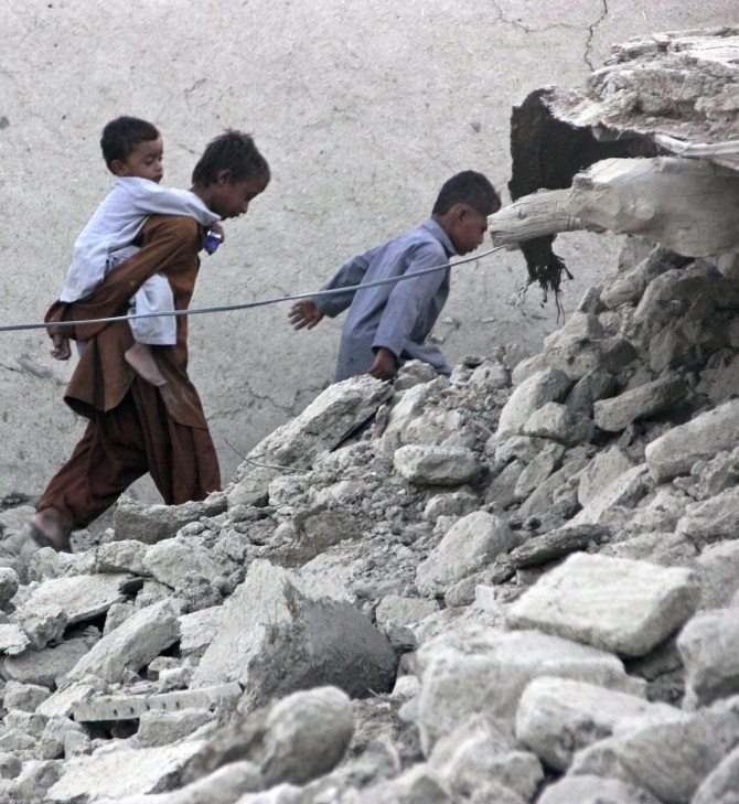 -Survivors of an earthquake walk on rubble of a mud house after it collapsed following the quake in the town of Awaran