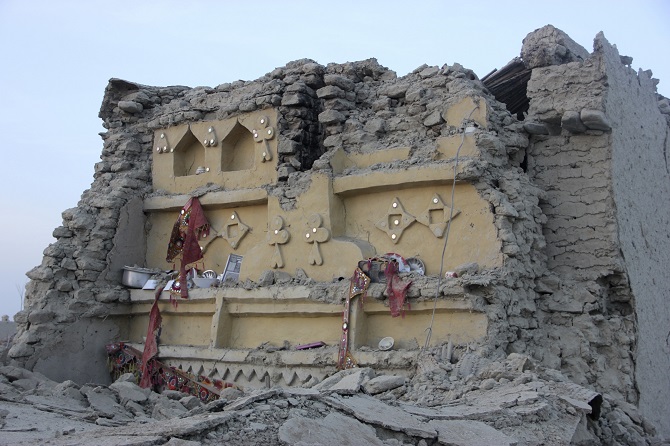 A survivor of an earthquake sits in the rubble of his mud house