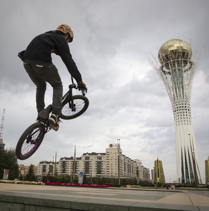 A teenager rides a bicycle near the Baiterek in Astana